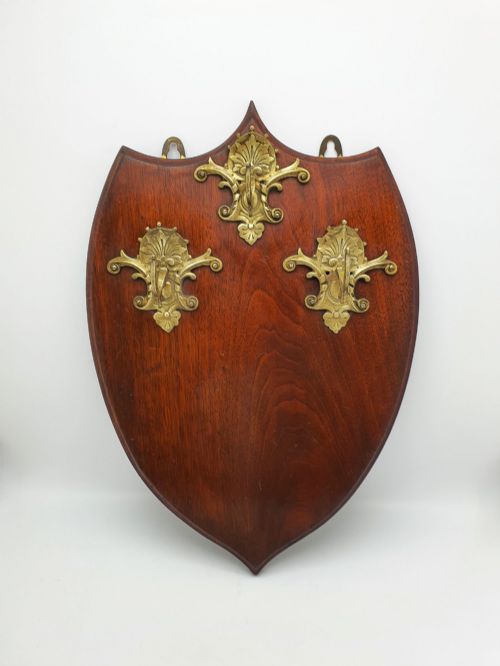 fig 2. A shield-shaped mahogany wall plaque equipped with three decorative cast brass coat hooks arranged symmetrically.
