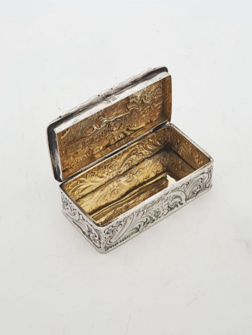 fig 1. A rectangular Victorian sterling silver snuff box with intricate repousse relief work depicting a pastoral scene surrounded by floral scrollwork.
