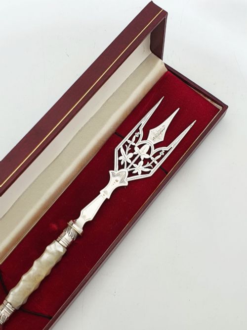 fig 1. An Edwardian sterling silver bread fork featuring pierced foliage tines and a carved mother-of-pearl handle resting inside a red fitted box.
