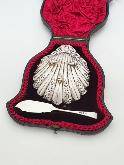 fig 2. A Victorian sterling silver scallop shell butter dish and matching engraved spreader knife resting inside a fitted red and black velvet presentation case.