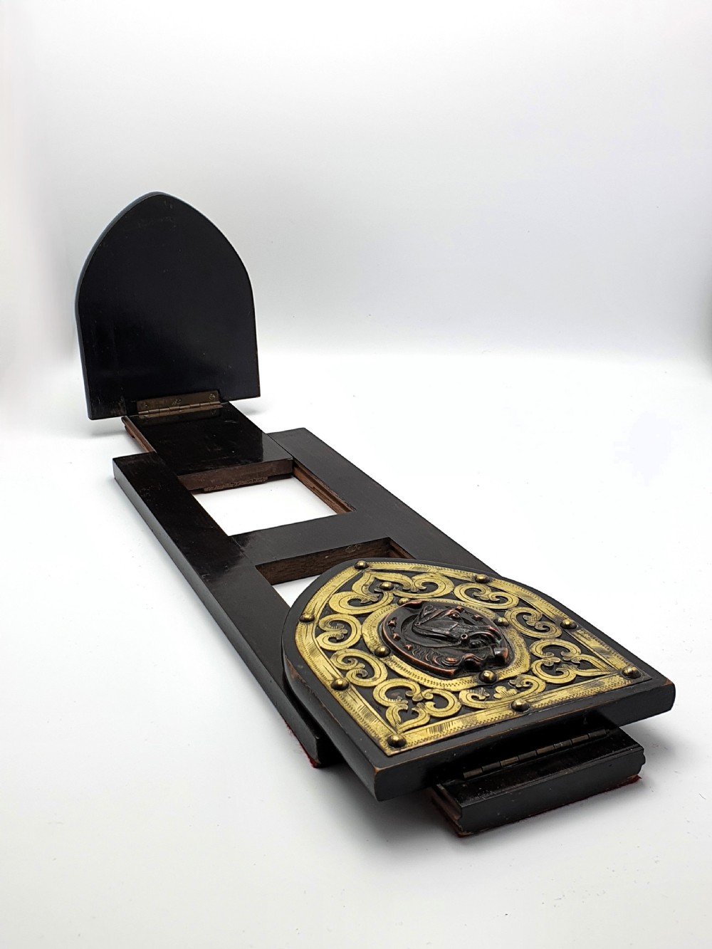 An ebonised wooden expanding book slide featuring pointed arched folding ends decorated with engraved brass straps and a central copper horseshoe medallion with a horse profile. View V