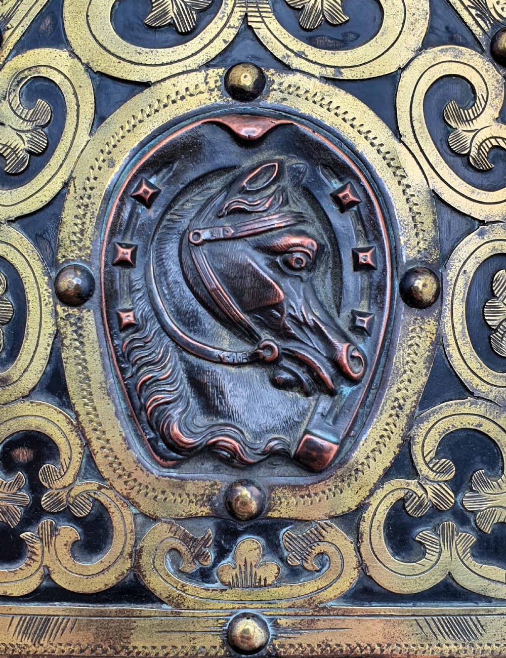 An ebonised wooden expanding book slide featuring pointed arched folding ends decorated with engraved brass straps and a central copper horseshoe medallion with a horse profile. View VI