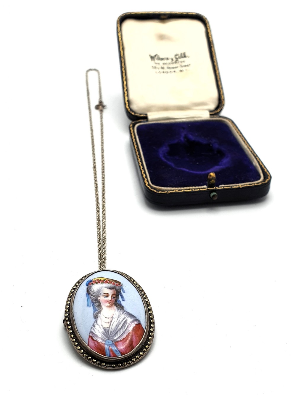 An oval silver pendant brooch featuring a hand-painted portrait of an eighteenth-century woman, presented inside a blue velvet box. View II