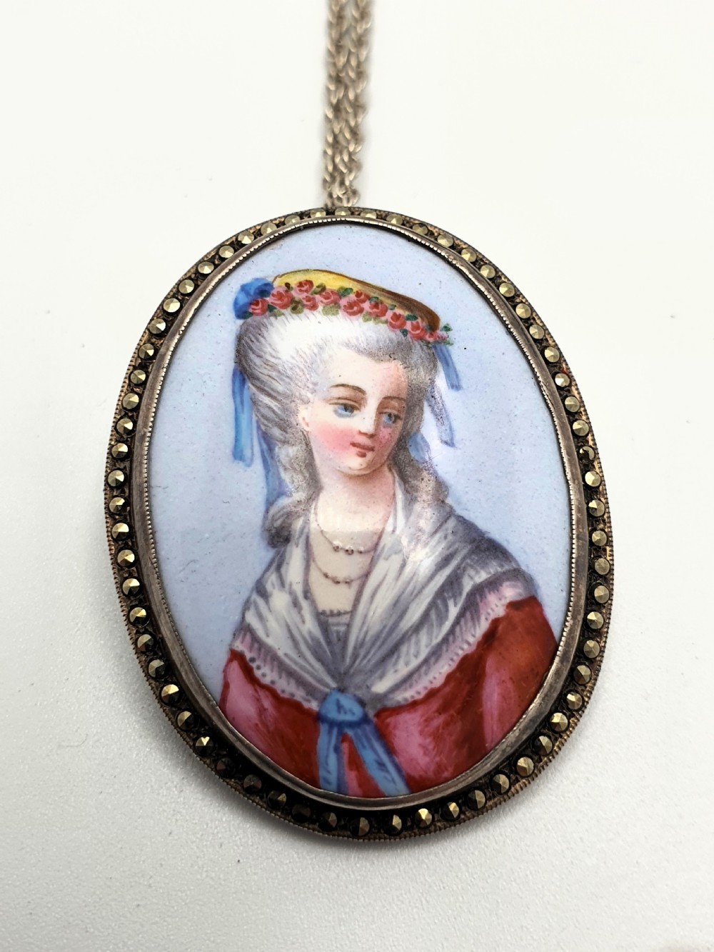 An oval silver pendant brooch featuring a hand-painted portrait of an eighteenth-century woman, presented inside a blue velvet box. View III
