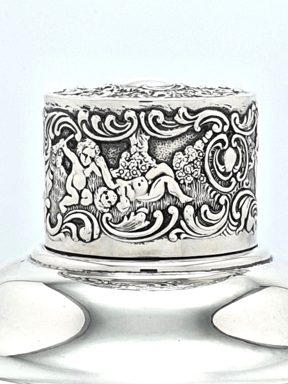 An antique clear glass cocktail shaker featuring etched silver overlay foliage patterns and relief-carved sterling silver mounts depicting cherubs. View V