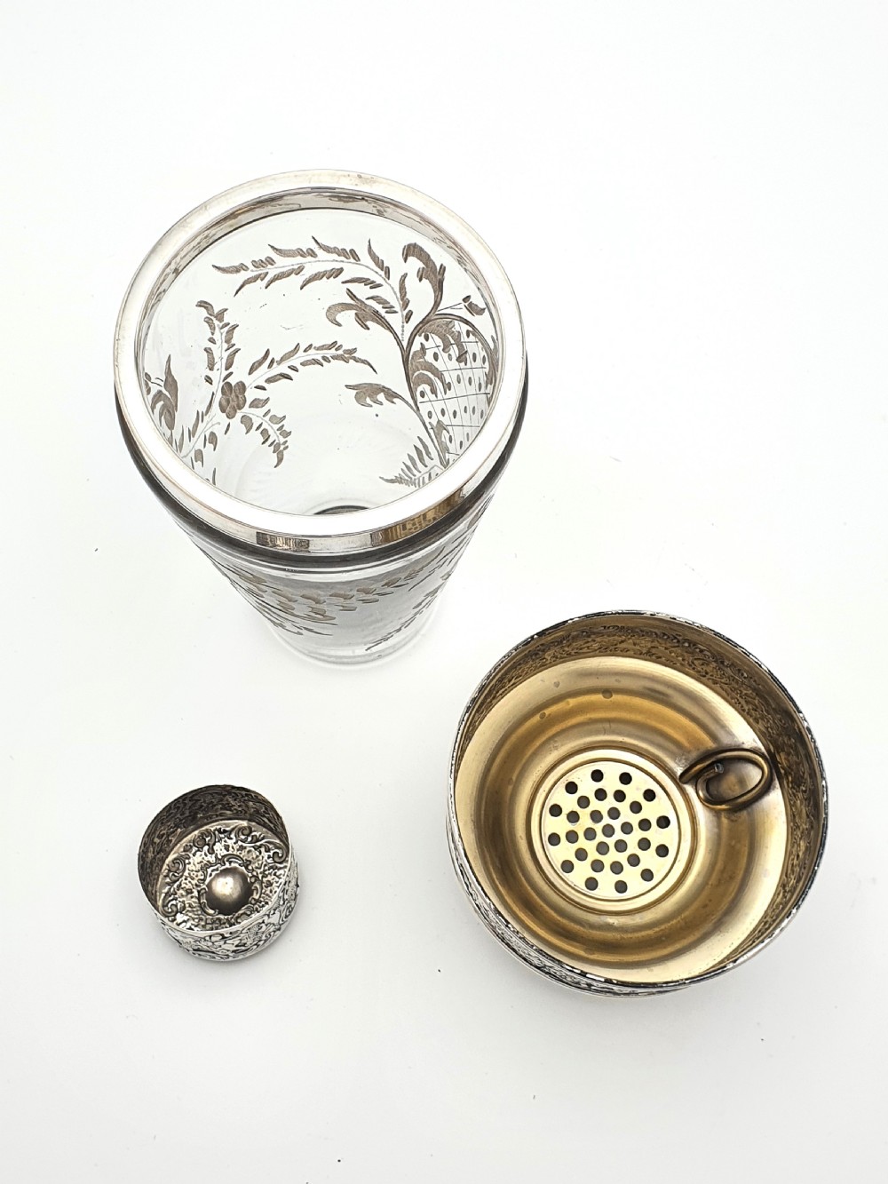 An antique clear glass cocktail shaker featuring etched silver overlay foliage patterns and relief-carved sterling silver mounts depicting cherubs. View VIII