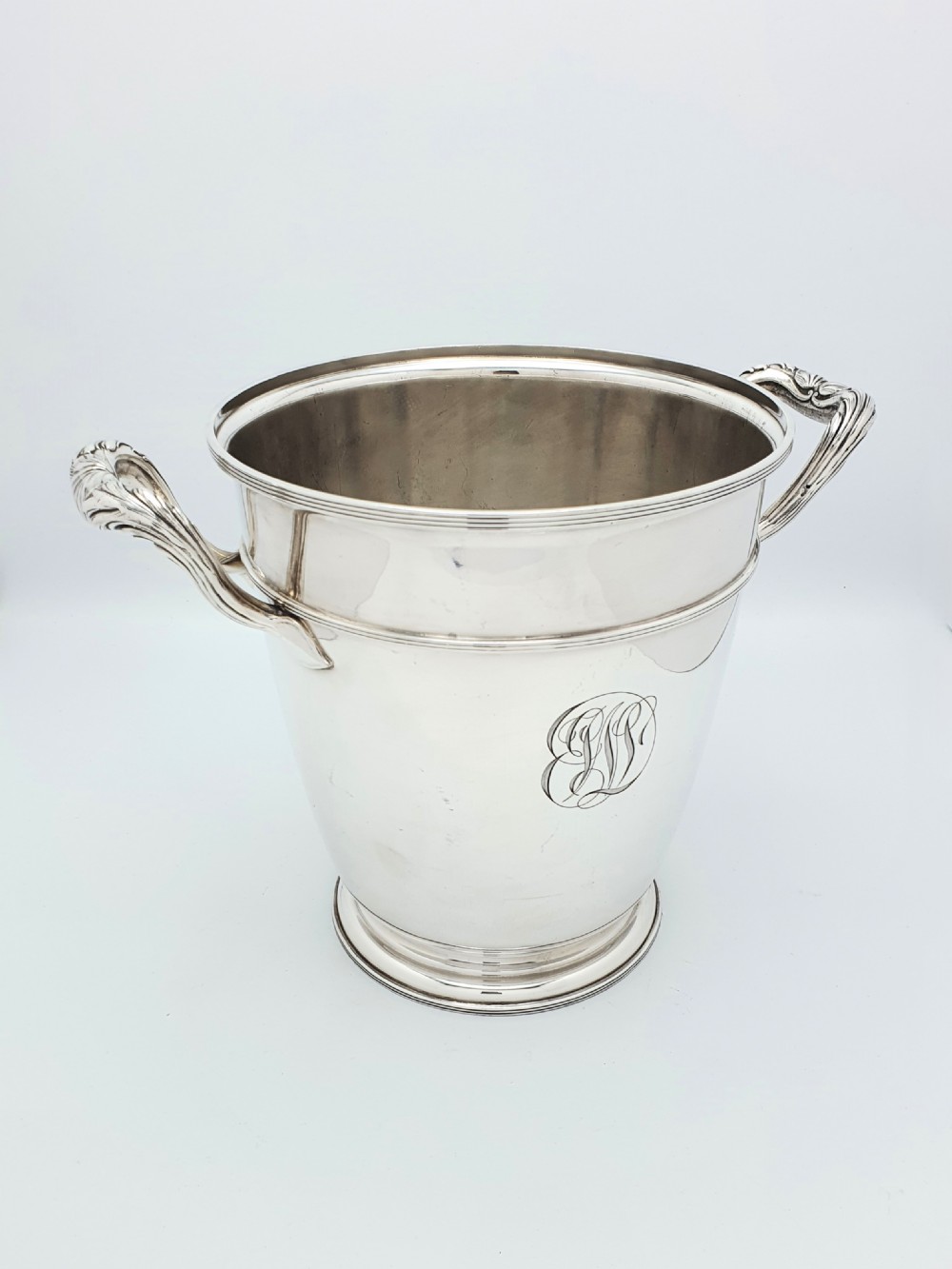 A silver-plated champagne bucket featuring twin side handles, a moulded rim, and an engraved script monogram on the front.