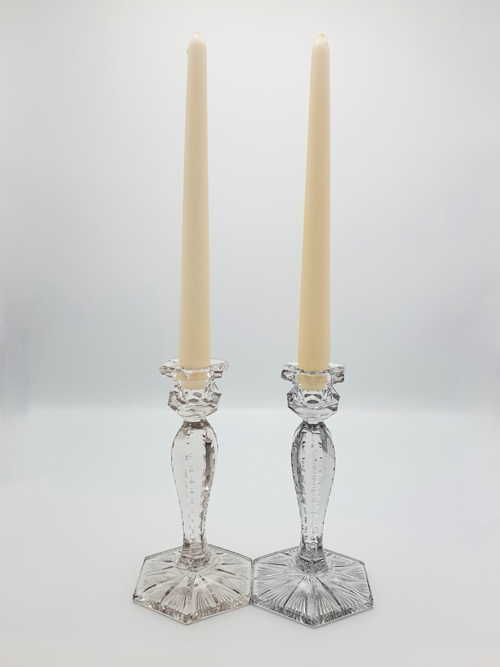 A pair of clear cut-glass candlesticks featuring faceted stems and starburst hexagonal bases holding tall cream taper candles.