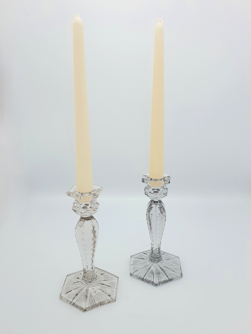 A pair of clear cut-glass candlesticks featuring faceted stems and starburst hexagonal bases holding tall cream taper candles. View II
