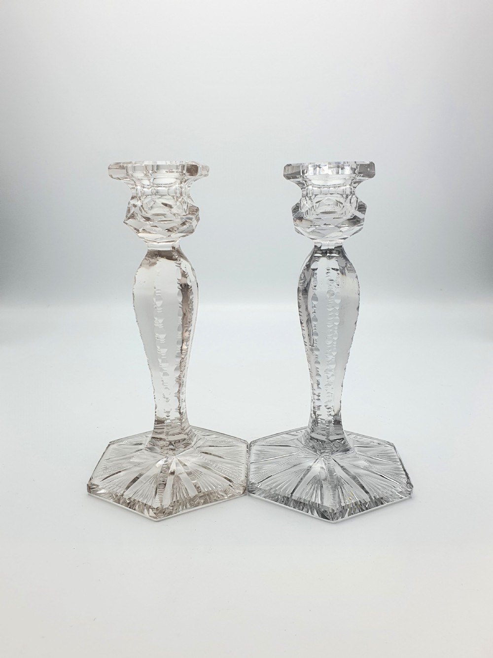 A pair of clear cut-glass candlesticks featuring faceted stems and starburst hexagonal bases holding tall cream taper candles. View IV