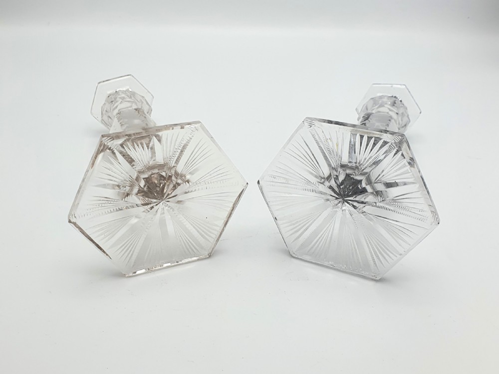 A pair of clear cut-glass candlesticks featuring faceted stems and starburst hexagonal bases holding tall cream taper candles. View V