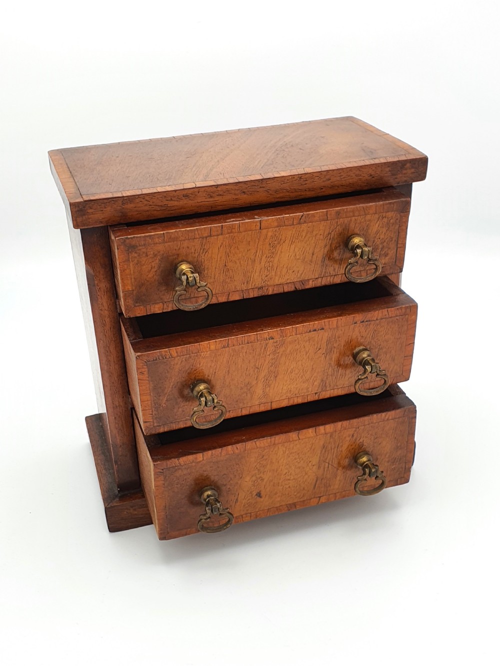 A small mahogany three-drawer miniature chest with brass drop handles and inlaid wood banding. View II