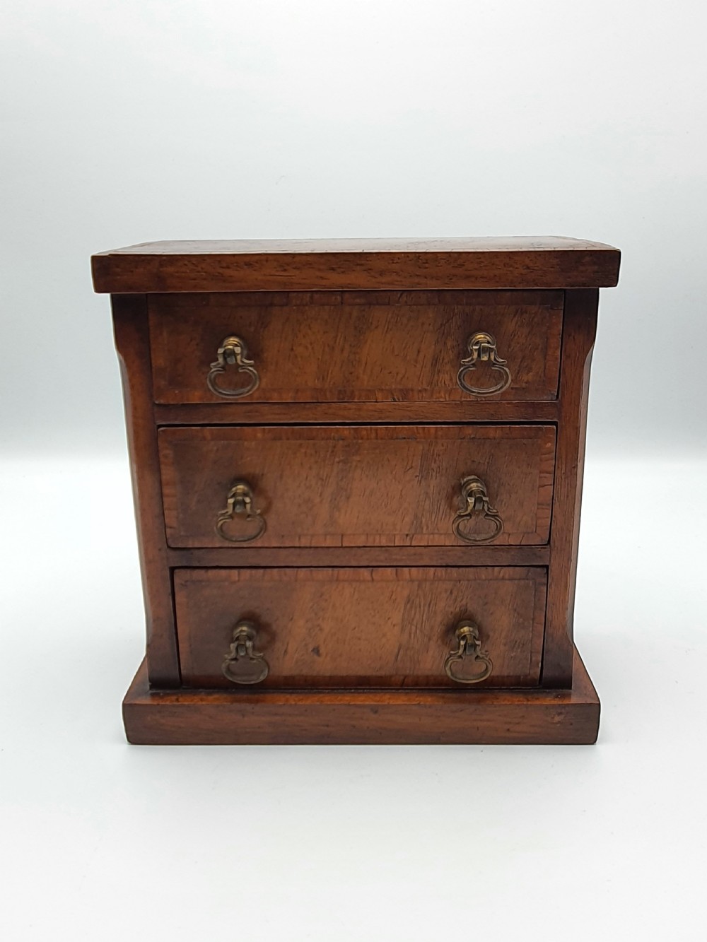 A small mahogany three-drawer miniature chest with brass drop handles and inlaid wood banding. View V