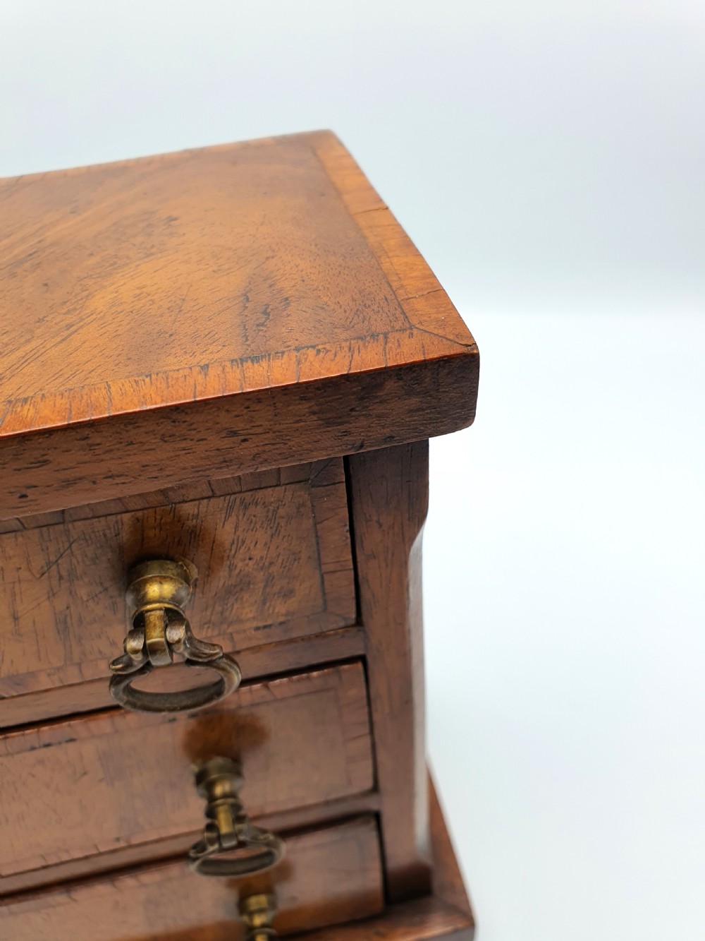 A small mahogany three-drawer miniature chest with brass drop handles and inlaid wood banding. View VII