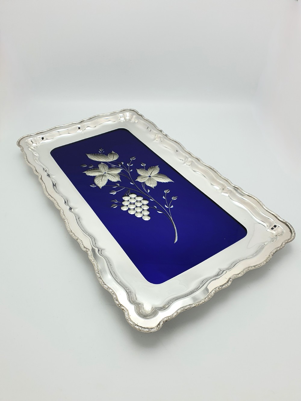 A rectangular silver-plated tray with a scalloped border featuring a deep cobalt blue glass mirror insert engraved with a grapevine and leaf motif. View III