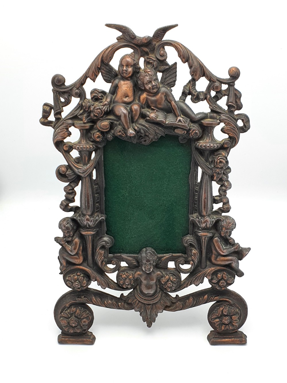 An ornate dark bronze Edwardian cast iron picture frame decorated with cherubs, miniature side columns, scrolling foliate detailings, and a green felt insert.