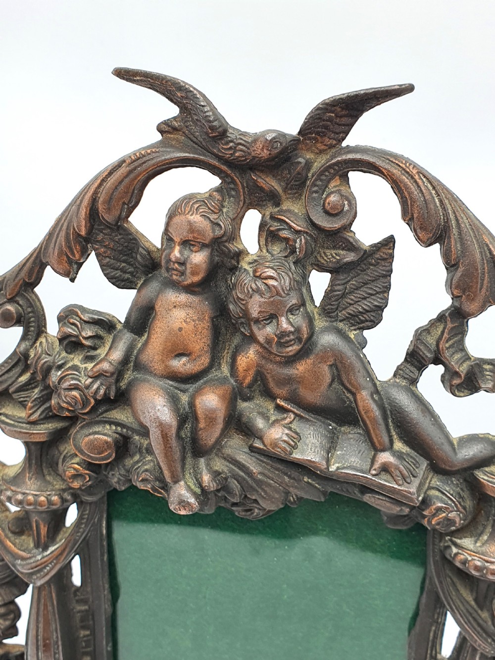 An ornate dark bronze Edwardian cast iron picture frame decorated with cherubs, miniature side columns, scrolling foliate detailings, and a green felt insert. View III