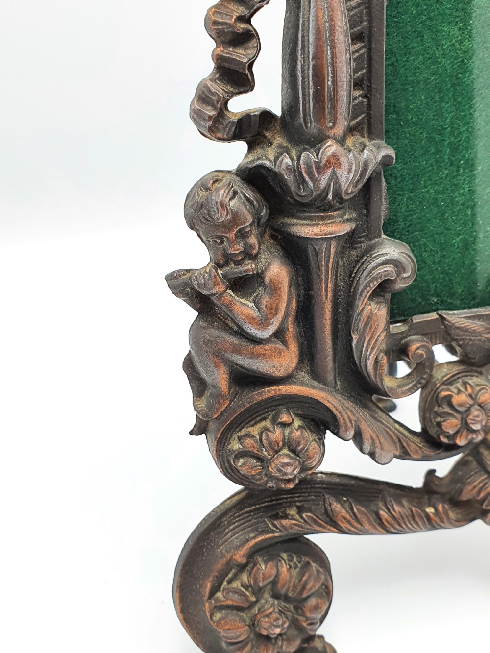 An ornate dark bronze Edwardian cast iron picture frame decorated with cherubs, miniature side columns, scrolling foliate detailings, and a green felt insert. View IV