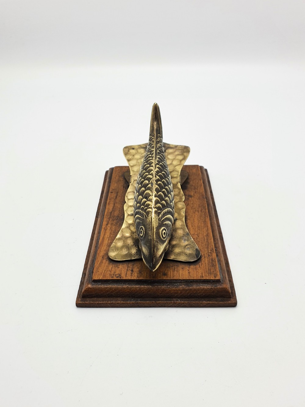 A 1920s brass fish-shaped spring clip mounted onto a molded rectangular wooden base. View IV