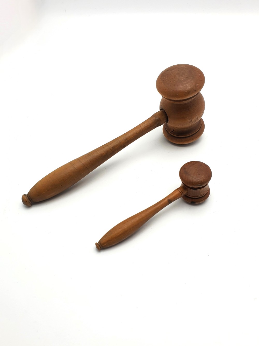 Two turned wooden gavels of differing sizes featuring cylindrical heads and shaped handles resting on a white background.