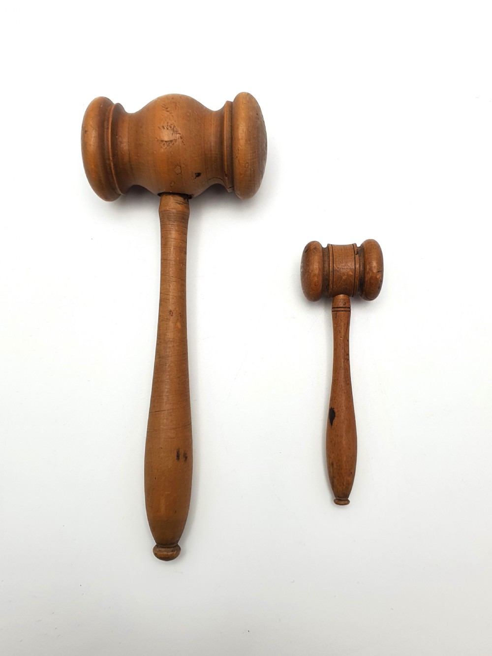 Two turned wooden gavels of differing sizes featuring cylindrical heads and shaped handles resting on a white background. View II