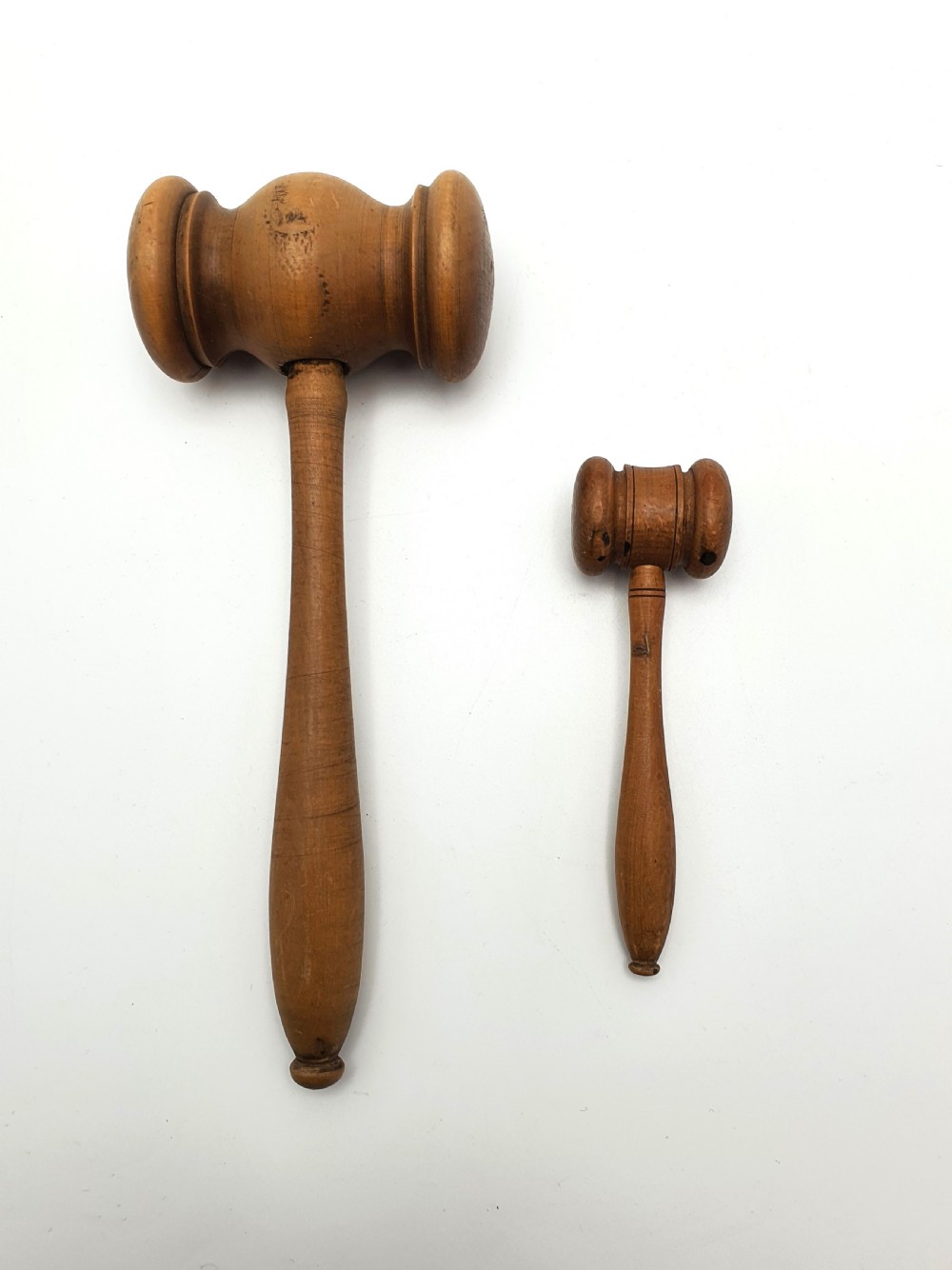 Two turned wooden gavels of differing sizes featuring cylindrical heads and shaped handles resting on a white background. View III