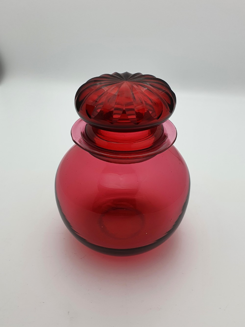 A spherical Edwardian cranberry red glass jar with a flanged neck and a faceted cut-glass stopper.
