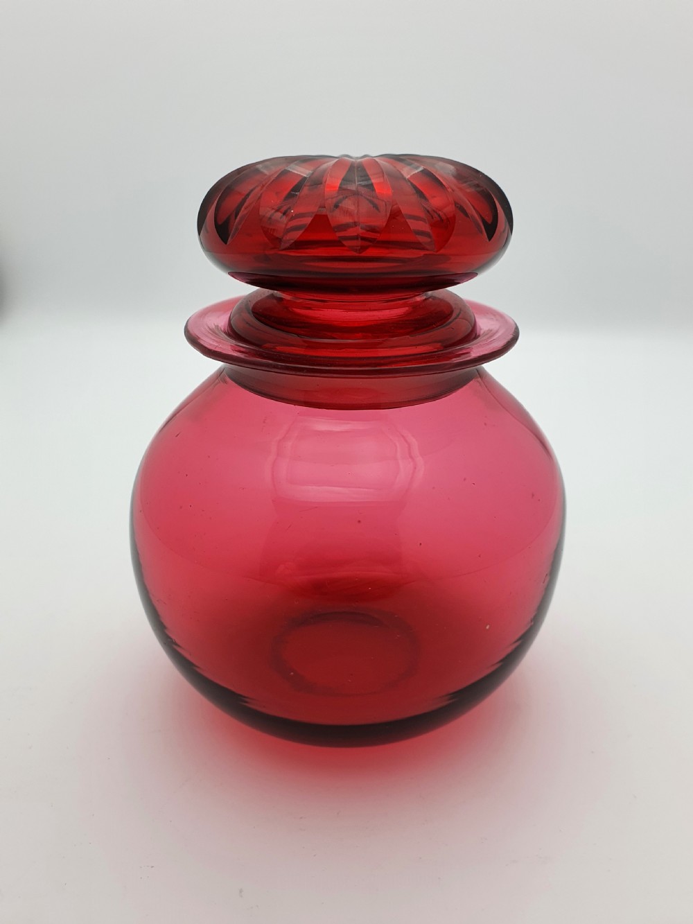 A spherical Edwardian cranberry red glass jar with a flanged neck and a faceted cut-glass stopper. View II