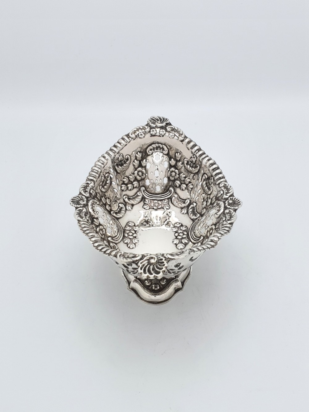 An ornate late Victorian pierced sterling silver basket featuring floral repousse ornamentation and a pedestal base.