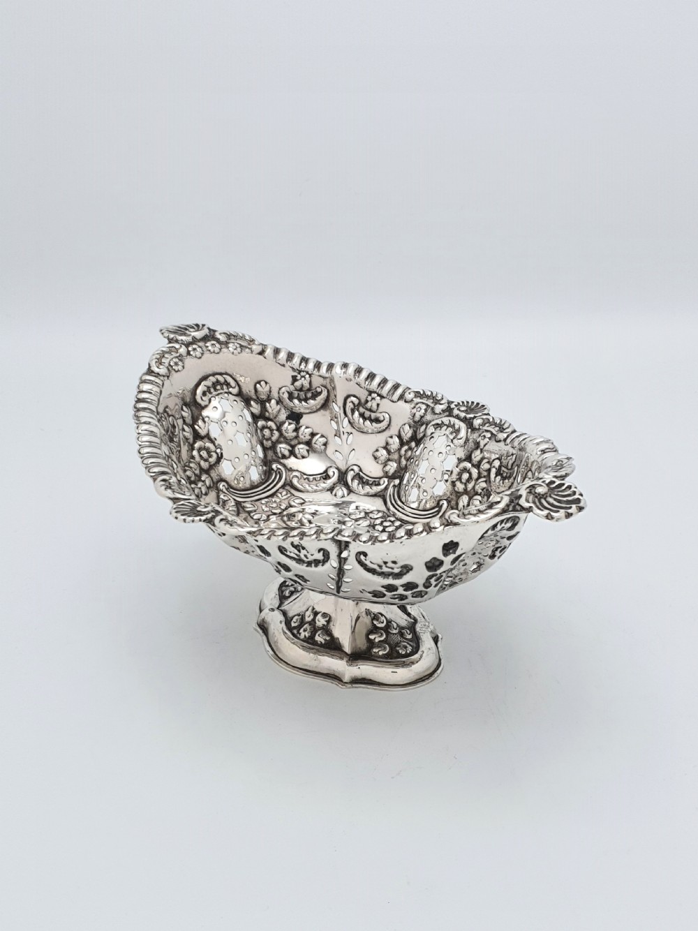 An ornate late Victorian pierced sterling silver basket featuring floral repousse ornamentation and a pedestal base. View II