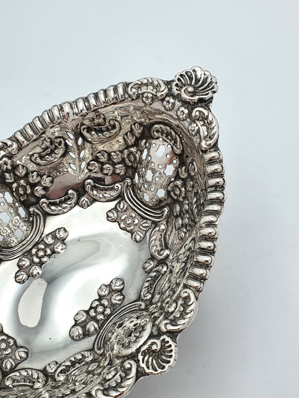 An ornate late Victorian pierced sterling silver basket featuring floral repousse ornamentation and a pedestal base. View V