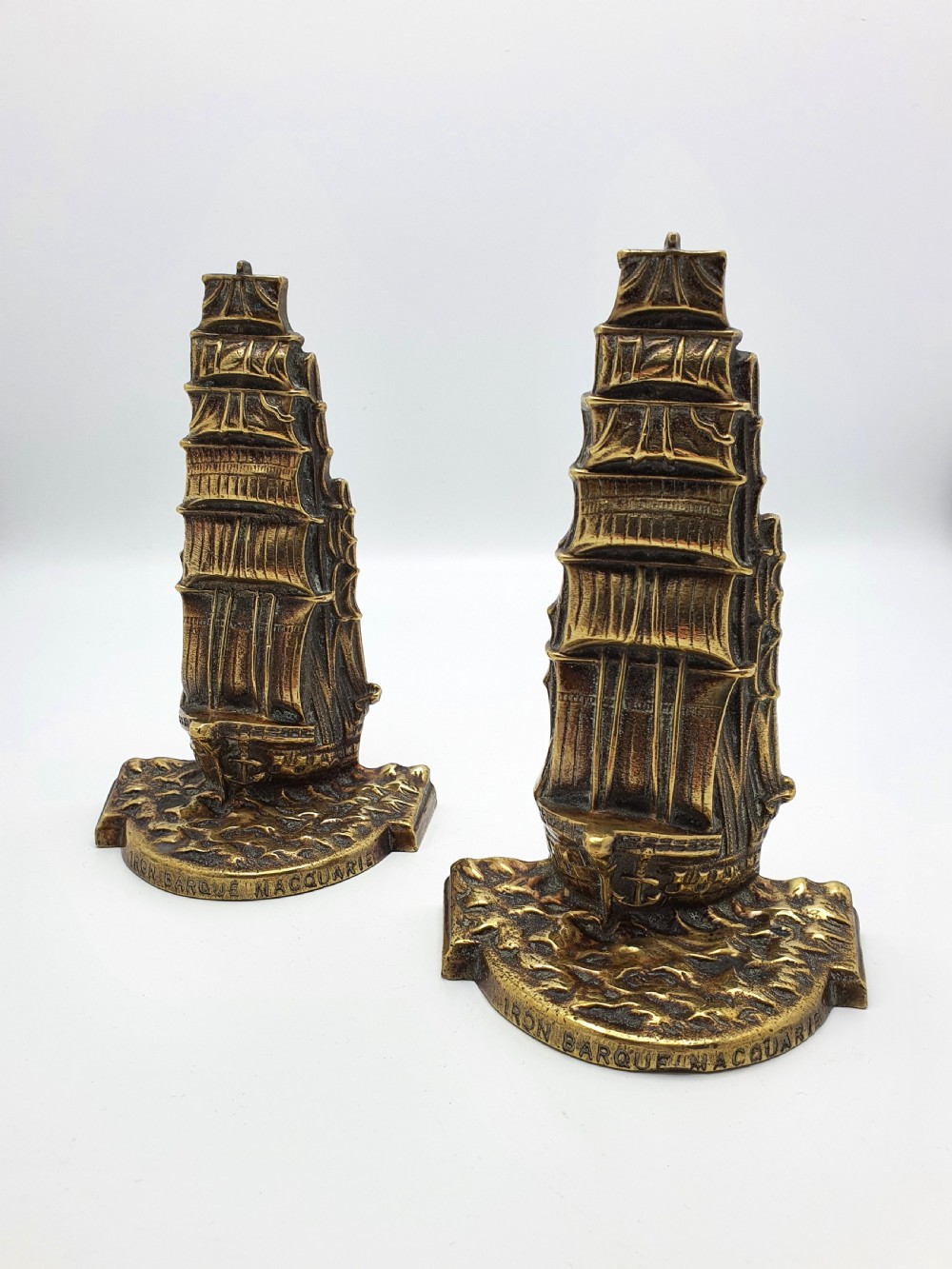 A pair of solid brass bookends featuring a relief design of a tall sailing ship on ocean waves.