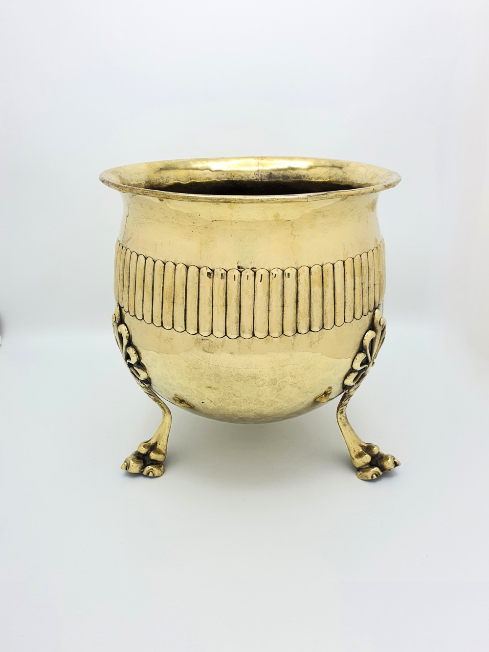 A rounded Edwardian brass jardiniere with a flared rim, a reeded central band, and three decorative cast feet.