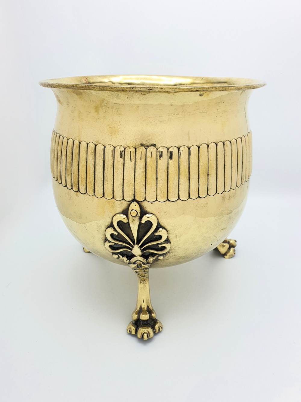 A rounded Edwardian brass jardiniere with a flared rim, a reeded central band, and three decorative cast feet. View II