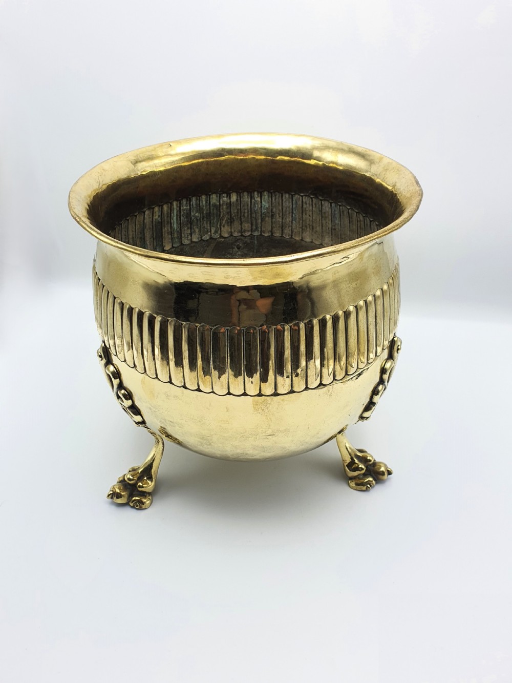 A rounded Edwardian brass jardiniere with a flared rim, a reeded central band, and three decorative cast feet. View V