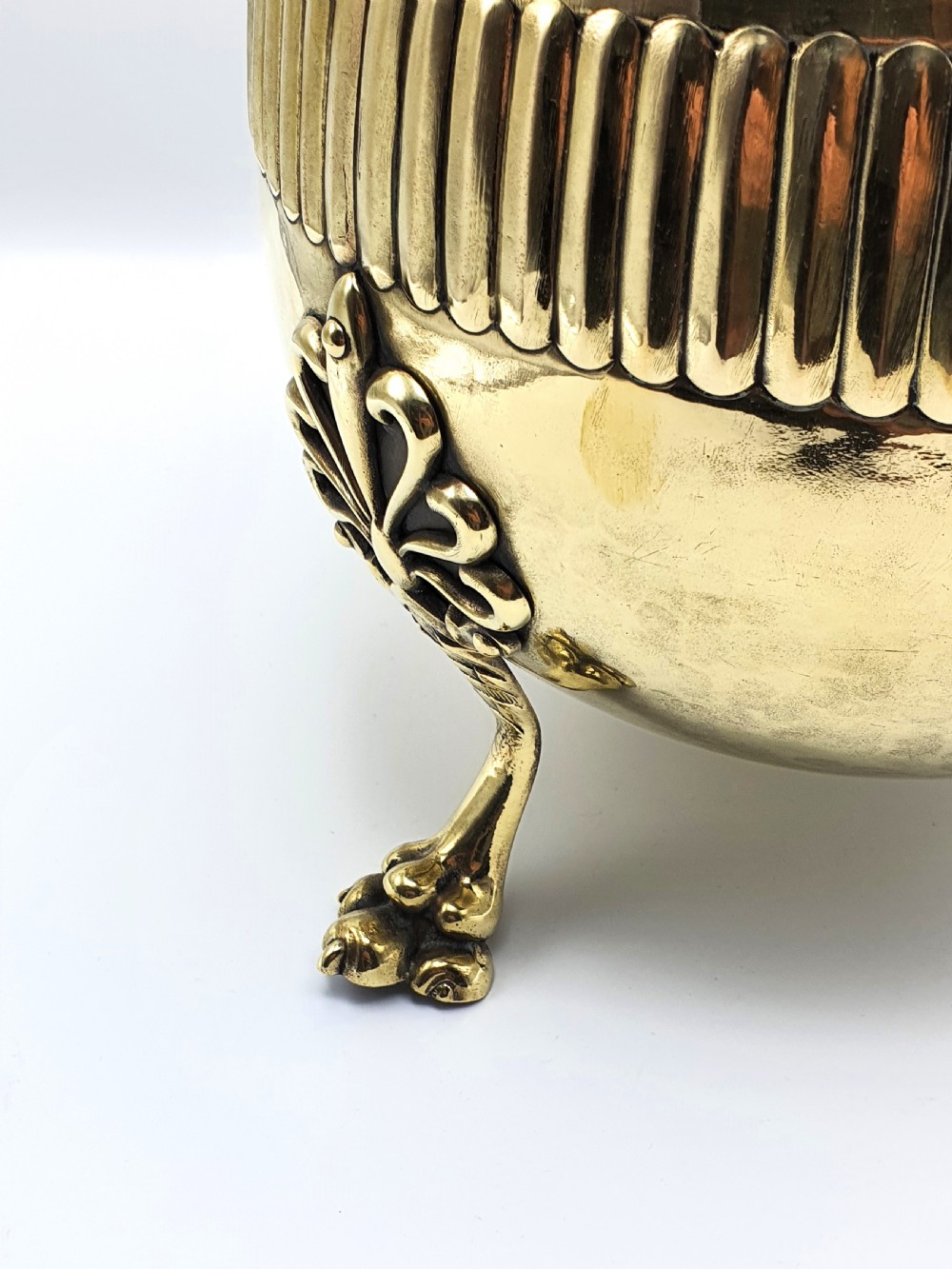 A rounded Edwardian brass jardiniere with a flared rim, a reeded central band, and three decorative cast feet. View VI