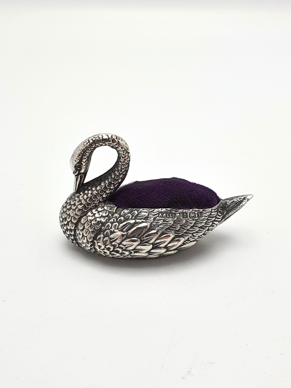 A hallmarked Edwardian sterling silver pin cushion crafted in the shape of a swan with detailed feather moulding and a purple velvet insert.