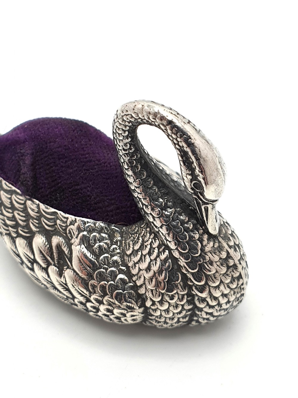 A hallmarked Edwardian sterling silver pin cushion crafted in the shape of a swan with detailed feather moulding and a purple velvet insert. View VI