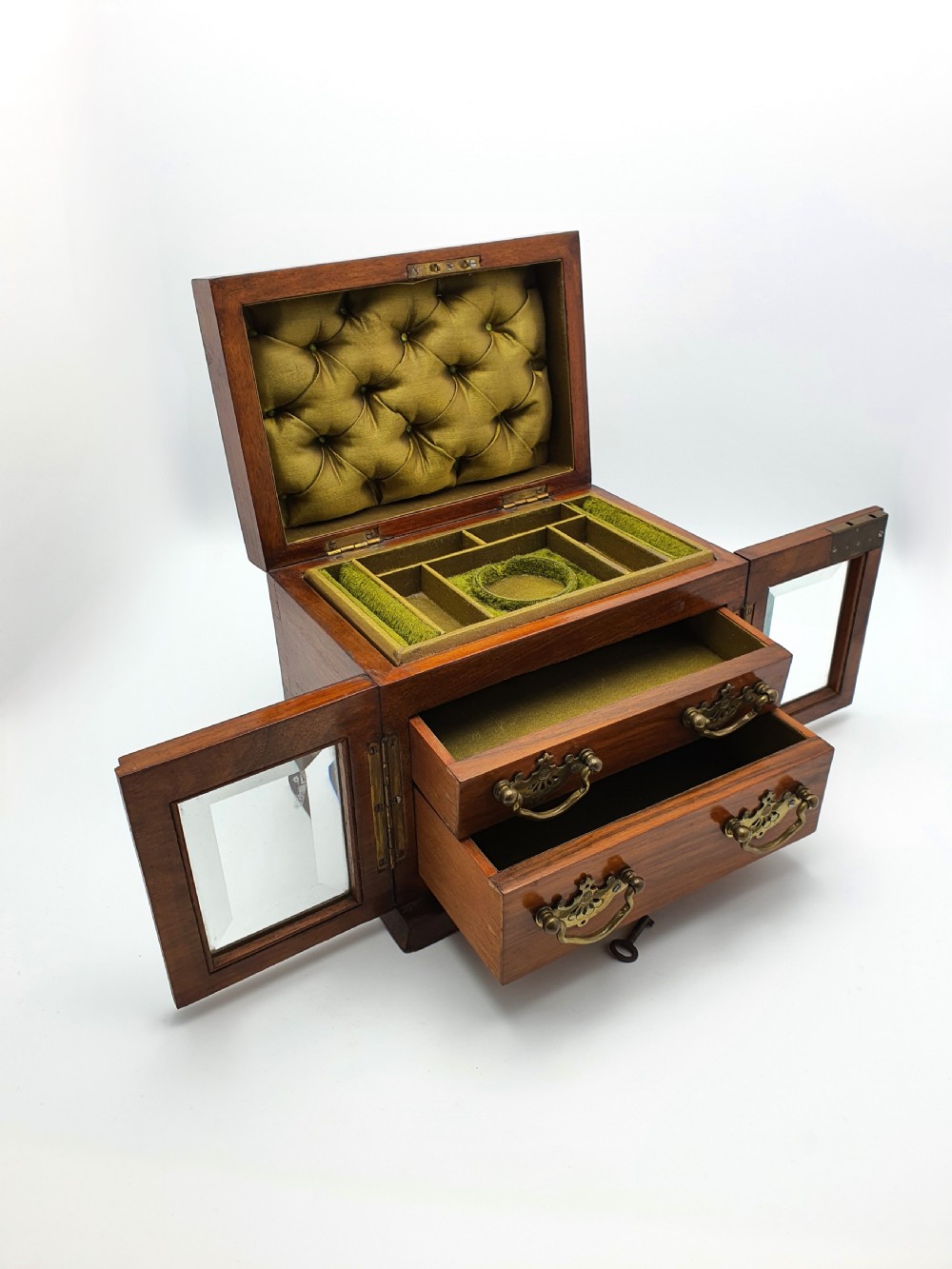 A Victorian walnut jewellery chest with open glass-panelled side doors, two pull-out drawers with brass handles, and an open lid revealing a button-tufted green velvet interior.