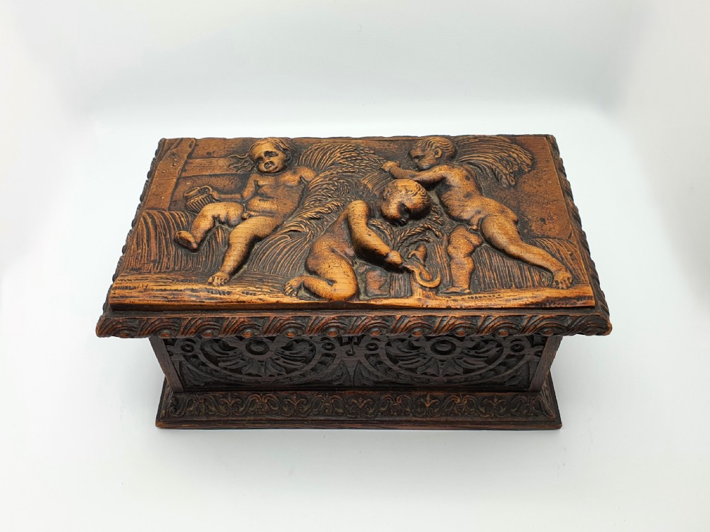 A Victorian dark oak tea caddy featuring detailed relief carvings of cherubs on the lid and carved scrollwork around the sides. View II