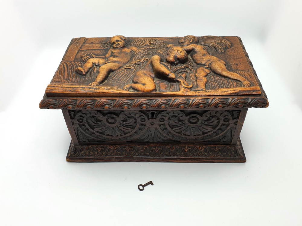 A Victorian dark oak tea caddy featuring detailed relief carvings of cherubs on the lid and carved scrollwork around the sides. View III