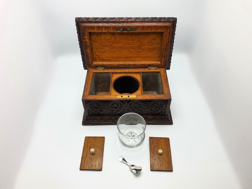 A Victorian dark oak tea caddy featuring detailed relief carvings of cherubs on the lid and carved scrollwork around the sides. View V