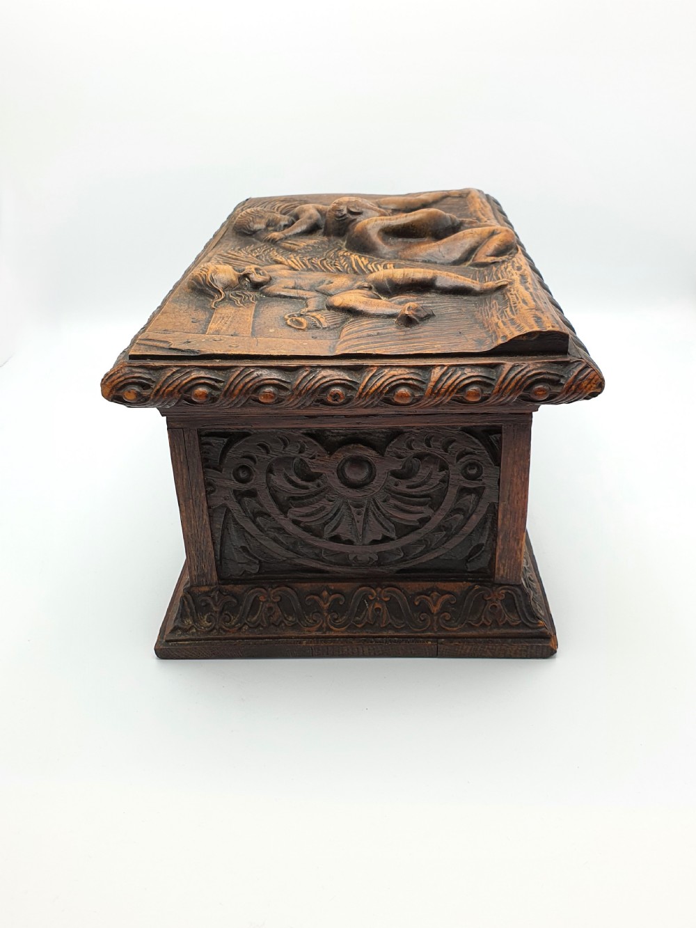 A Victorian dark oak tea caddy featuring detailed relief carvings of cherubs on the lid and carved scrollwork around the sides. View VI
