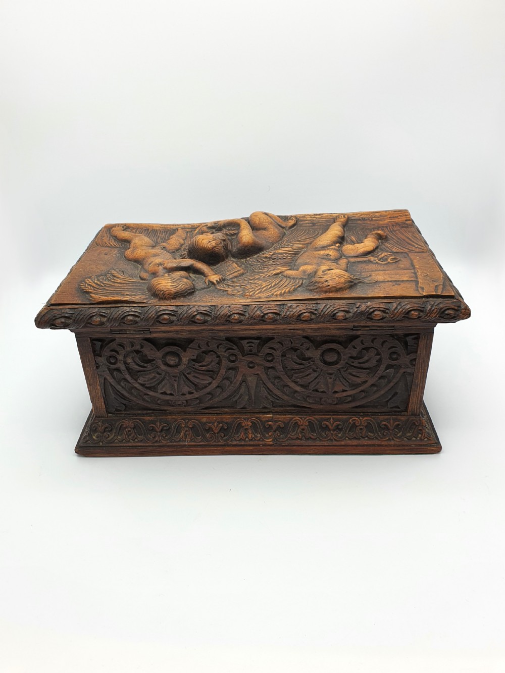 A Victorian dark oak tea caddy featuring detailed relief carvings of cherubs on the lid and carved scrollwork around the sides. View VII