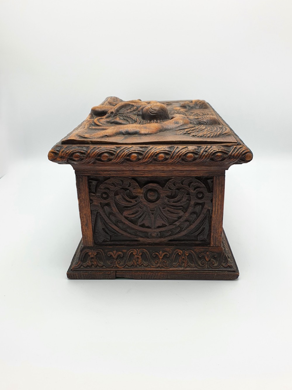 A Victorian dark oak tea caddy featuring detailed relief carvings of cherubs on the lid and carved scrollwork around the sides. View VIII