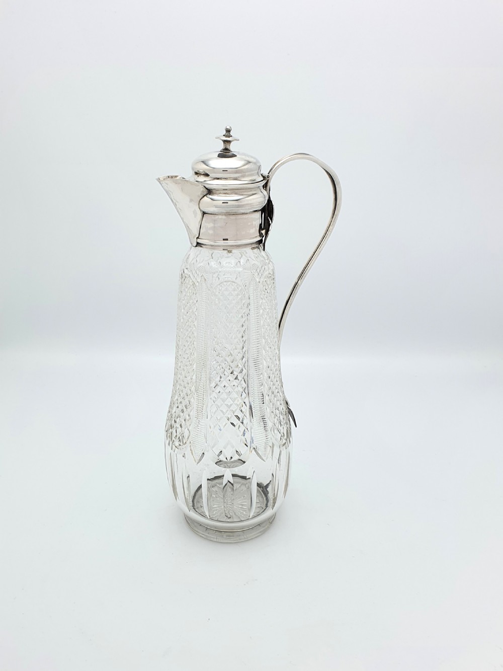 An antique Arts and Crafts period claret jug featuring a diamond-cut glass body with a silver-plated mount, hinged lid, and curved handle. View II