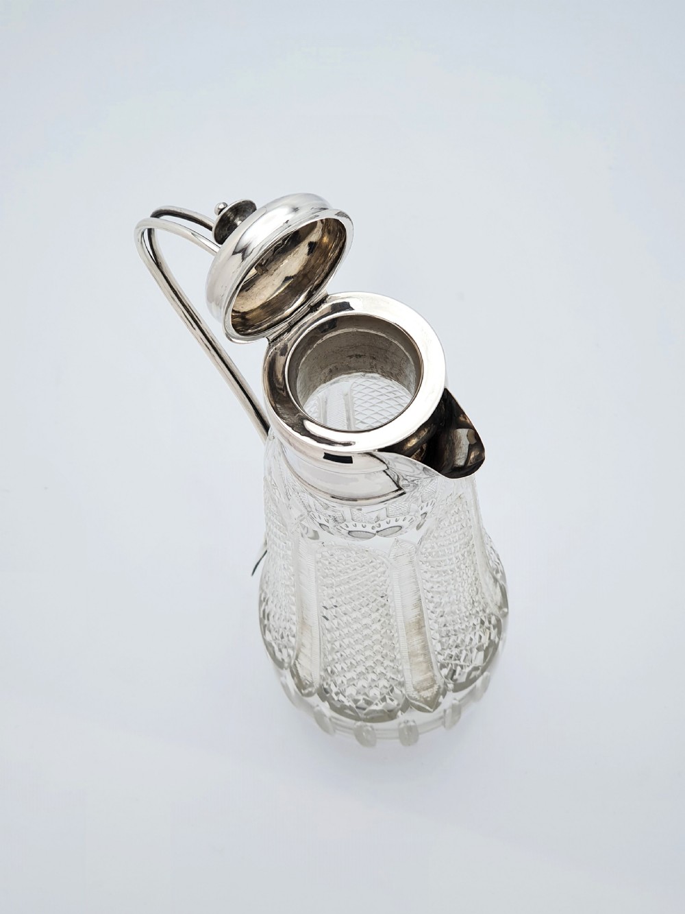 An antique Arts and Crafts period claret jug featuring a diamond-cut glass body with a silver-plated mount, hinged lid, and curved handle. View III