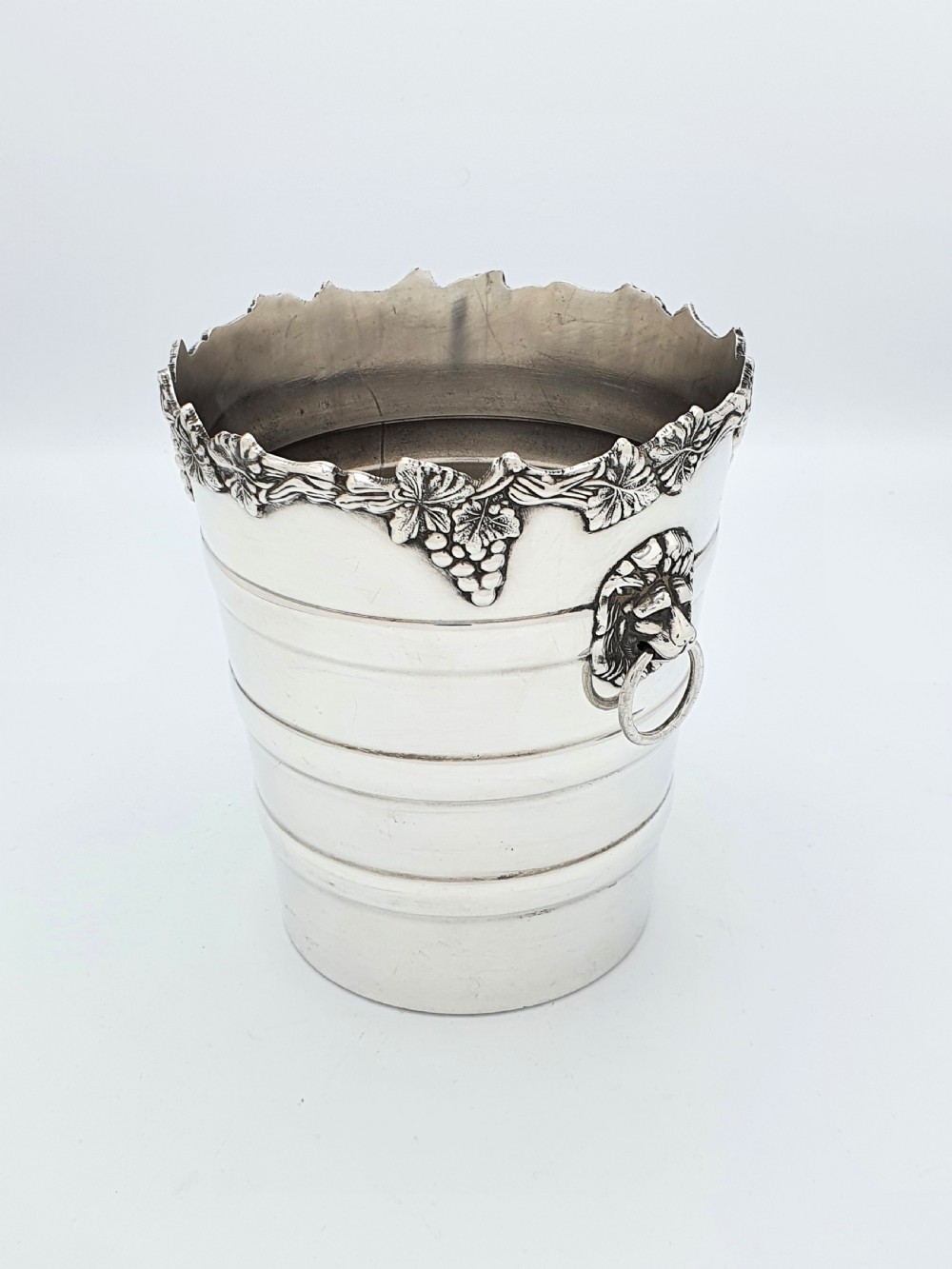 A tapered silver-plated wine bucket featuring a scalloped rim decorated with grapevine relief and lion head mask ring handles.
