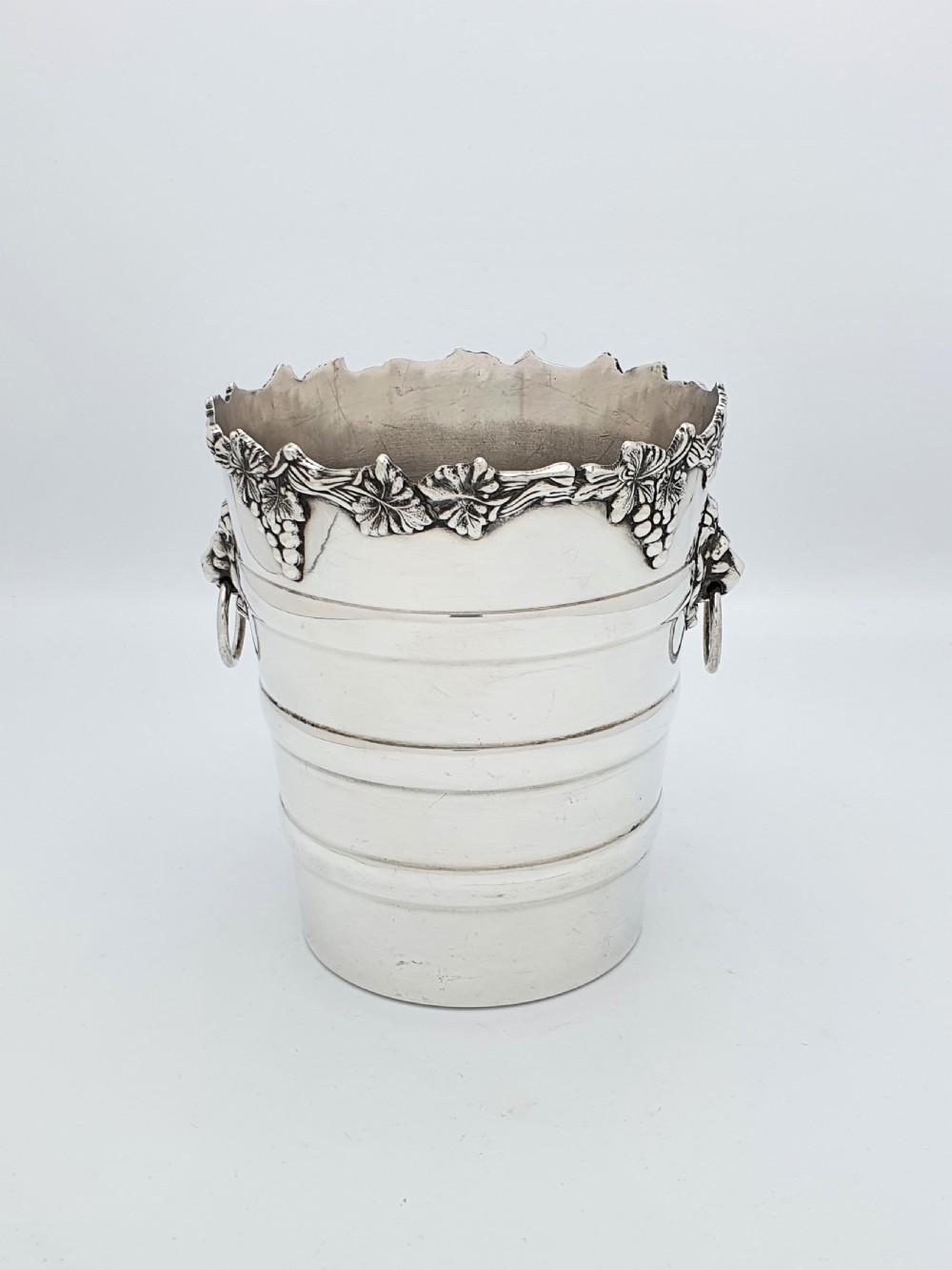 A tapered silver-plated wine bucket featuring a scalloped rim decorated with grapevine relief and lion head mask ring handles. View II