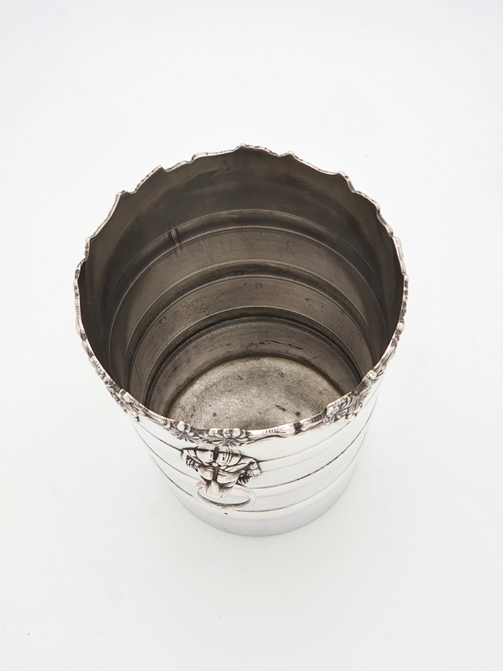 A tapered silver-plated wine bucket featuring a scalloped rim decorated with grapevine relief and lion head mask ring handles. View V
